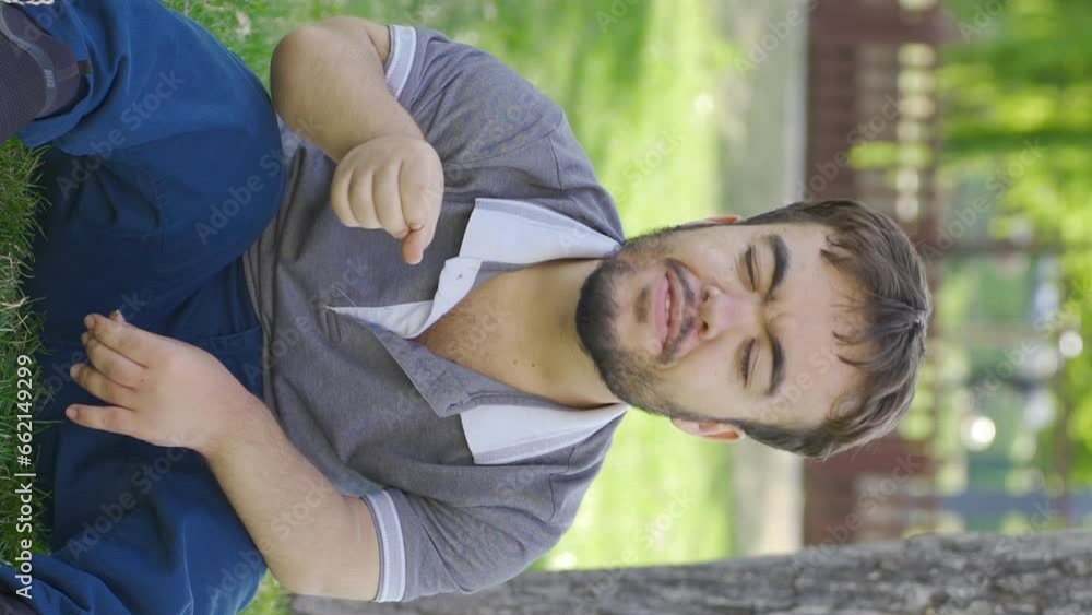 Vertical Video of Happy dwarf young man singing to himself in the park. Vertical Video of Happy dwarf young man singing to himself in the park.