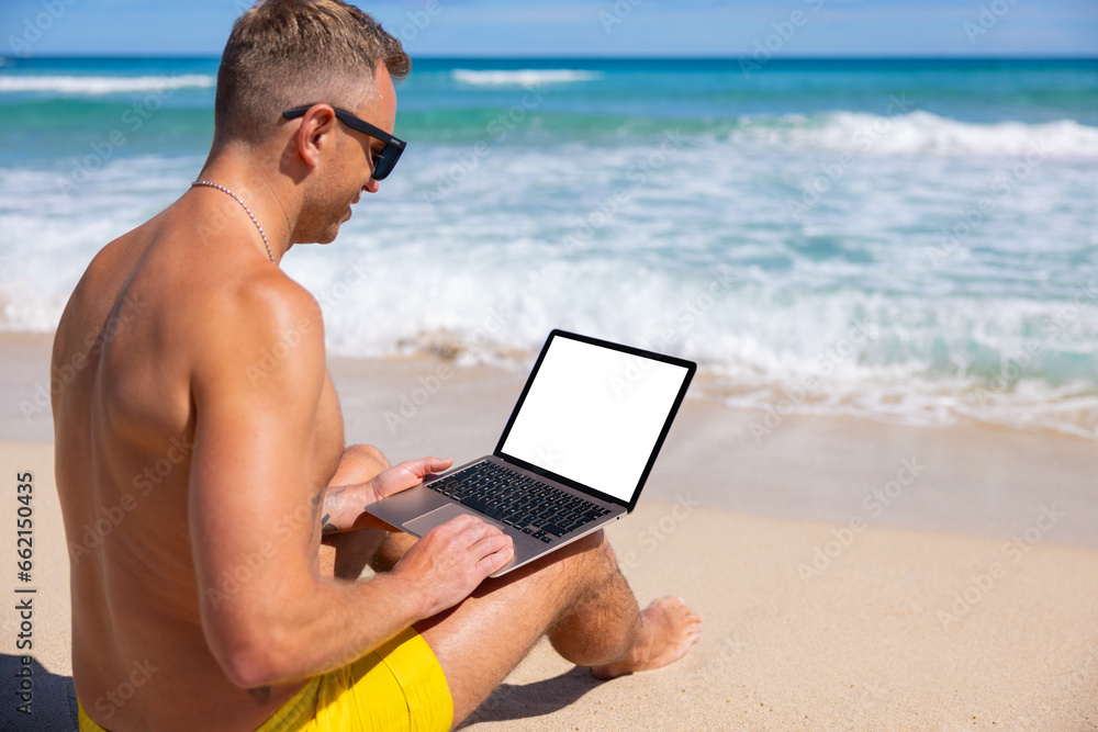 Man using laptop computer on the beach, white screen mockup