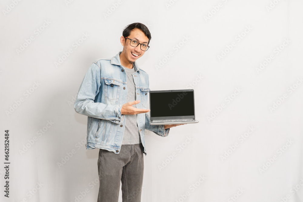 A man shows his laptop display with happy face. Indonesian or southeast asian model isolated with white wall background. A man shows his laptop display with happy face. Indonesian or southeast asian model isolated with white wall background.