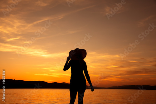 kobieta w kapeluszu na tle zachodzącego słońca nad morzem
