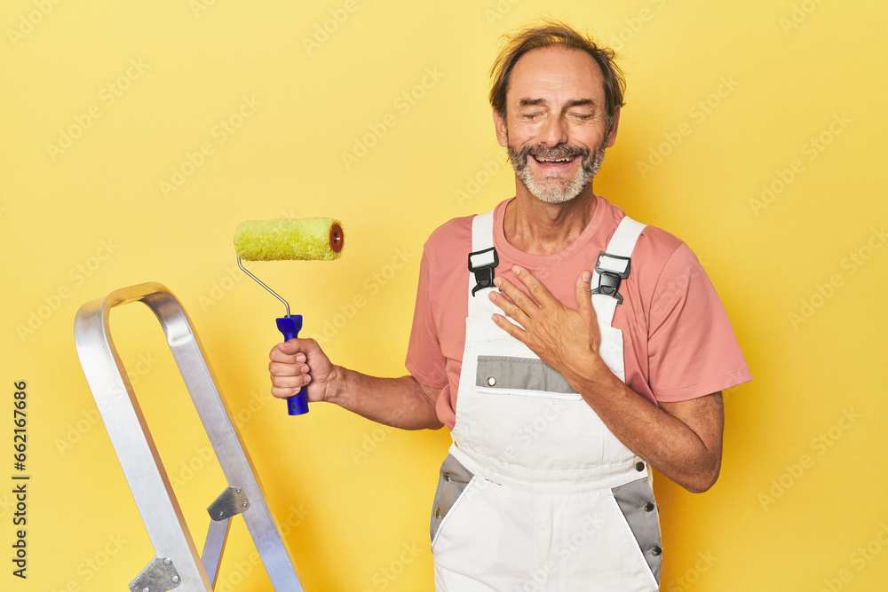 Man painting yellow backdrop in studio laughs out loudly keeping hand on chest. Man painting yellow backdrop in studio laughs out loudly keeping hand on chest.
