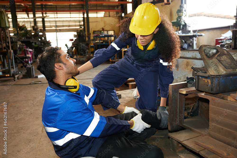factory worker or engineer suffering from knee pain and coworker getting first aids help in the factory factory worker or engineer suffering from knee pain and coworker getting first aids help in the factory
