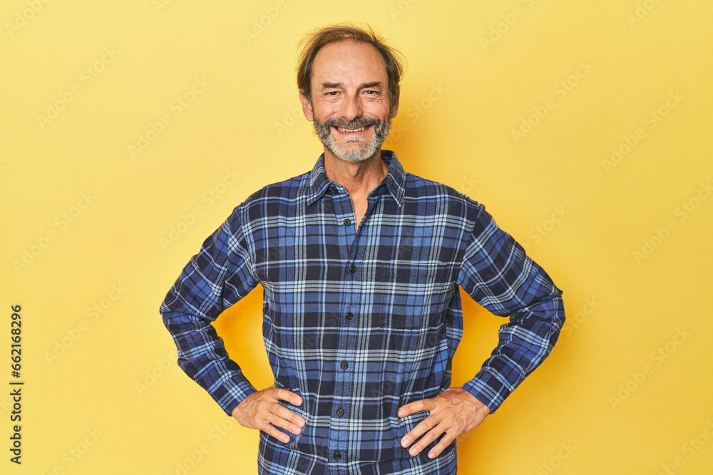 Caucasian middle-aged man in yellow studio confident keeping hands on hips. Caucasian middle-aged man in yellow studio confident keeping hands on hips.