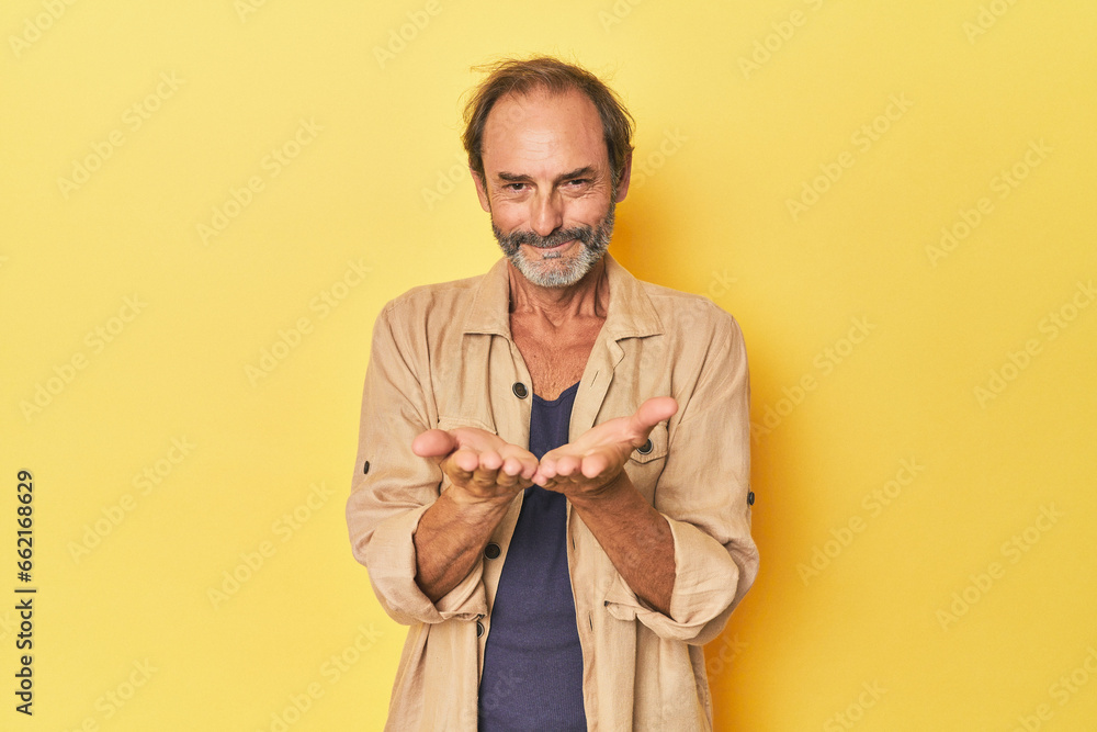 Obraz premium Caucasian middle-aged man in yellow studio holding something with palms, offering to camera.