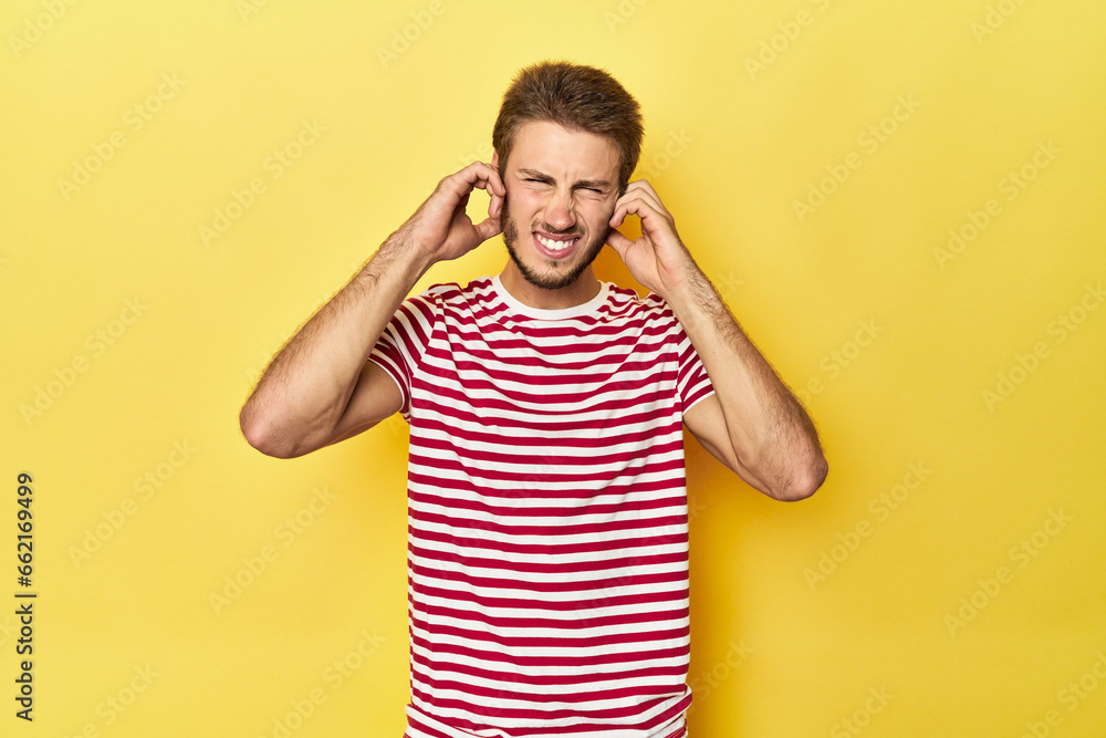 Young Caucasian man on a yellow studio background covering ears with hands. Young Caucasian man on a yellow studio background covering ears with hands.