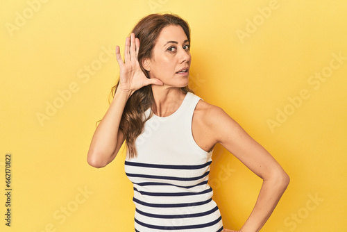 Middle-aged caucasian woman on yellow trying to listening a gossip.