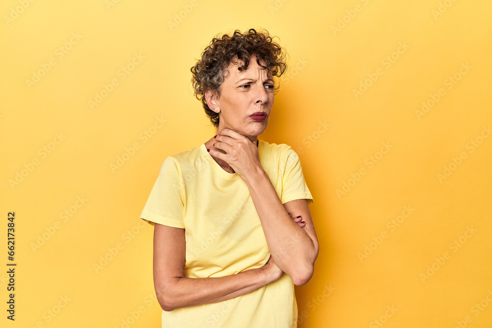 Mid-aged caucasian woman on vibrant yellow suffers pain in throat due a virus or infection.