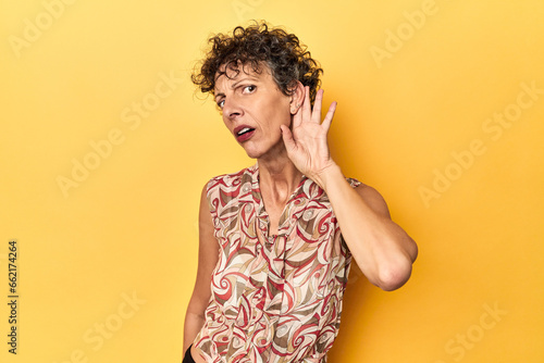 Mid-aged caucasian woman on vibrant yellow trying to listening a gossip.