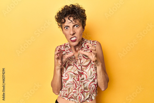 Mid-aged caucasian woman on vibrant yellow upset screaming with tense hands.