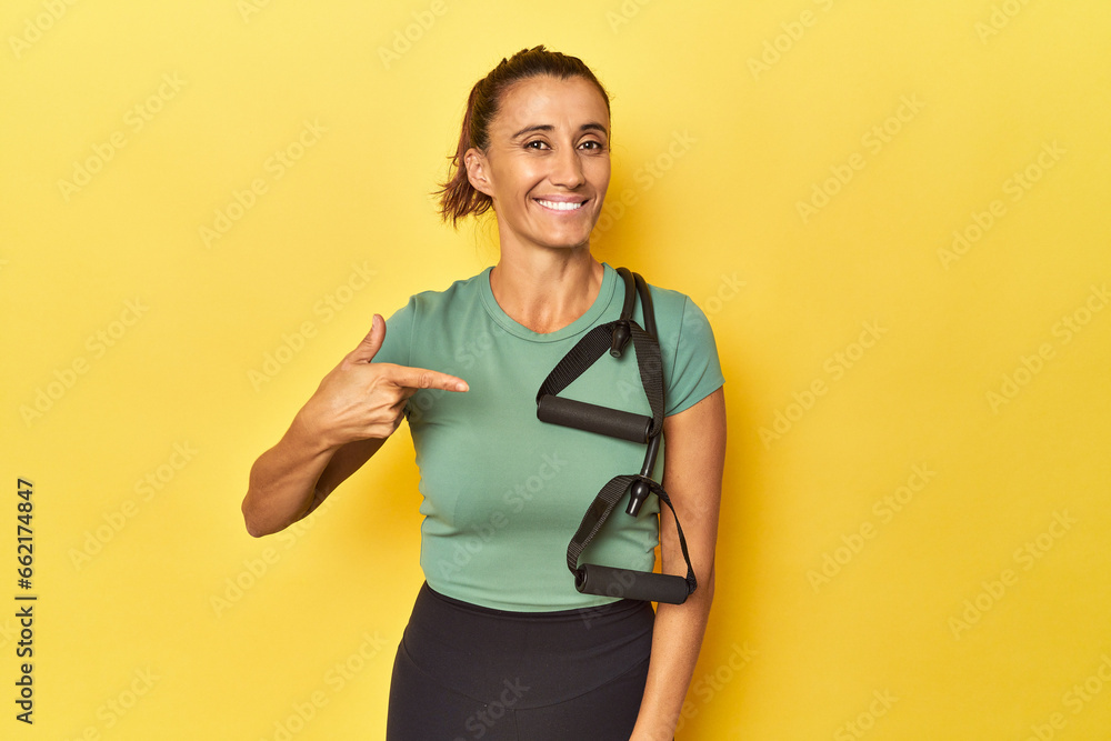 Middle aged sportswoman with resistance band on yellow person pointing by hand to a shirt copy space, proud and confident Middle aged sportswoman with resistance band on yellow person pointing by hand to a shirt copy space, proud and confident