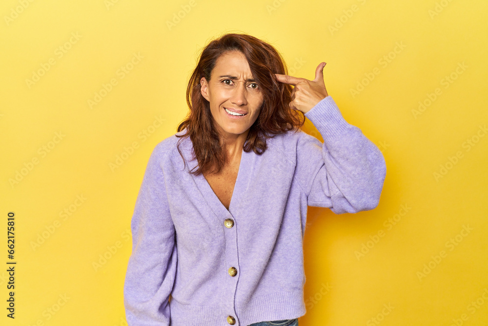 Middle-aged woman on a yellow backdrop showing a disappointment gesture with forefinger. Middle-aged woman on a yellow backdrop showing a disappointment gesture with forefinger.