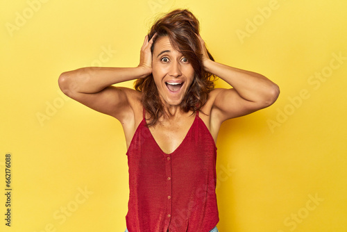 Middle-aged woman on a yellow backdrop screaming, very excited, passionate, satisfied with something.