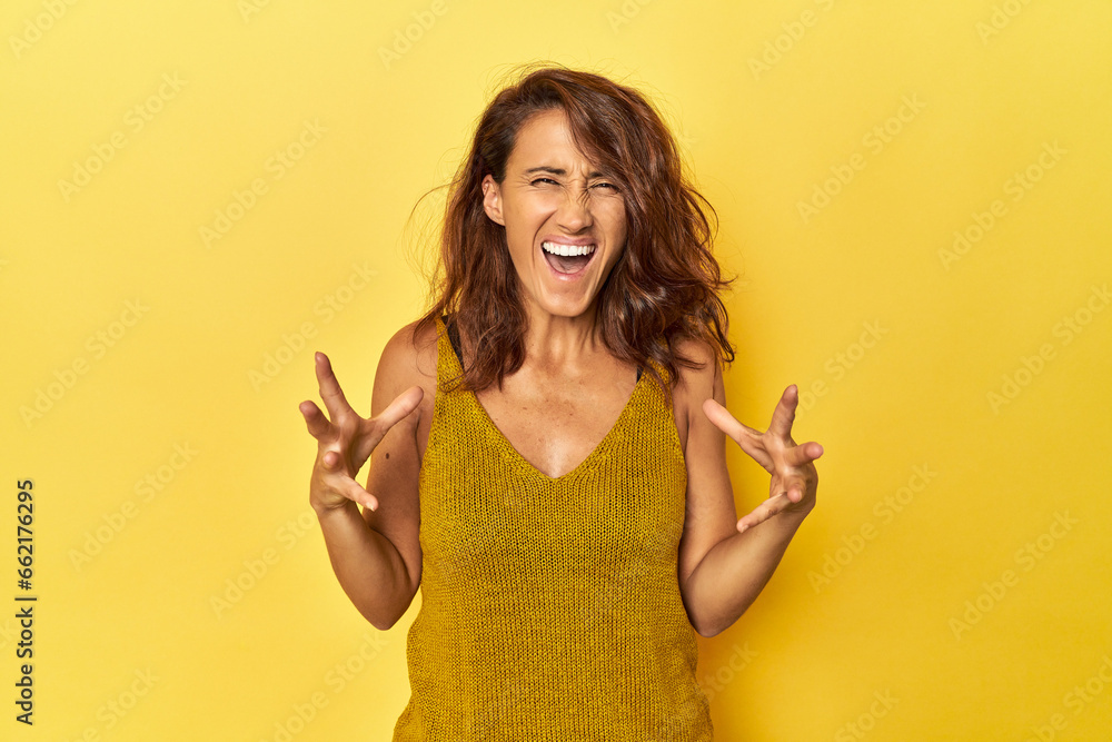 Middle-aged woman on a yellow backdrop screaming with rage. Middle-aged woman on a yellow backdrop screaming with rage.