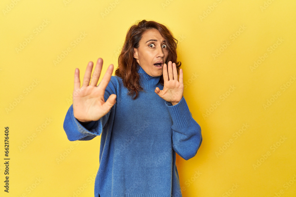 Middle-aged woman on a yellow backdrop being shocked due to an imminent danger Middle-aged woman on a yellow backdrop being shocked due to an imminent danger
