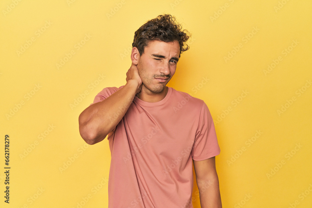 Young Latino man posing on yellow background having a neck pain due to stress, massaging and touching it with hand. Young Latino man posing on yellow background having a neck pain due to stress, massaging and touching it with hand.