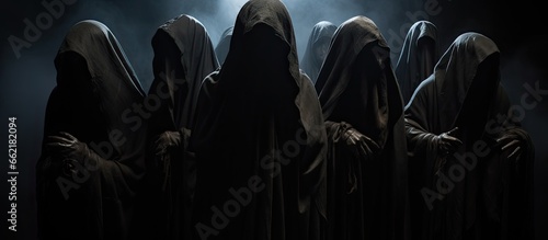 Nine mysterious figures in hooded cloaks in darkness With copyspace for text