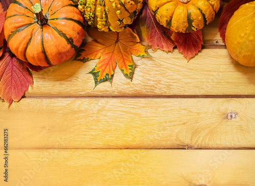 Autumn background: pumpkins and yellow and red leaves frame an ocher wooden table