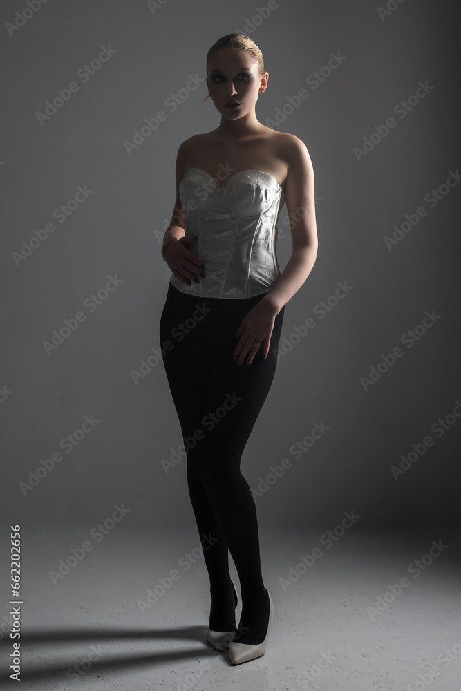 Beauty, fashion, style and make-up concept. Beautiful woman full body silhouette portrait. Part of model covered in shadow. Gray studio background. Model wearing white corset and high heels Beauty, fashion, style and make-up concept. Beautiful woman full body silhouette portrait. Part of model covered in shadow. Gray studio background. Model wearing white corset and high heels