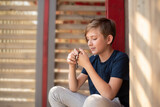 An 11 year old Catholic boy reads the rosary prayer, holds a wooden rosary with 10 beads in his hands. portrait of a boy with a wooden Catholic rosary during prayer.	
