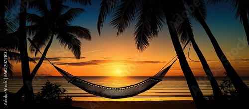 Hammock and palm trees on a tropical beach at sunset portrayed as a silhouette With copyspace for text