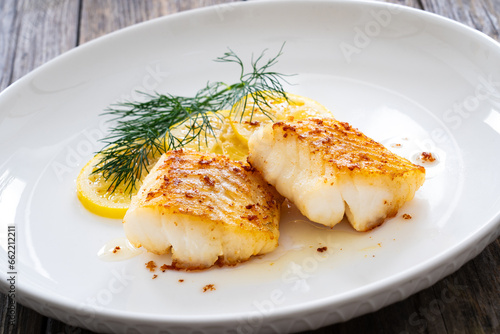 Seared cod loin and sliced lemon on wooden table

