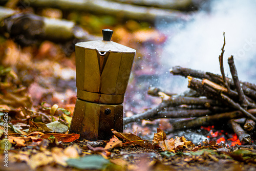 Percolator coffee pot near a blazing campfire with smoke, in the autumn forest, with fallen orange leaves.