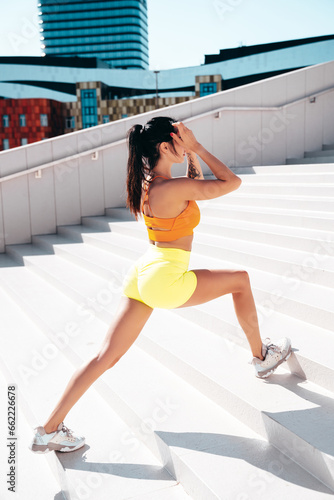 Fototapeta Naklejka Na Ścianę i Meble -  Fitness woman in sports clothing. Sexy young beautiful model athlete doing fitness workout. Female making exercises in the street at sunny day. Stretching out before training at stairs