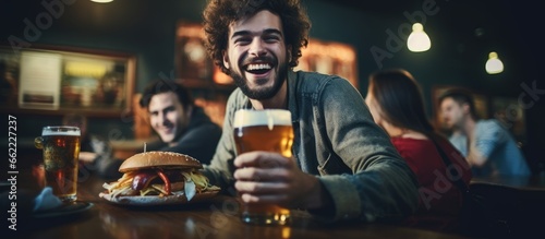 Joyful young man enjoying burgers and beer with friends at a pub With copyspace for text