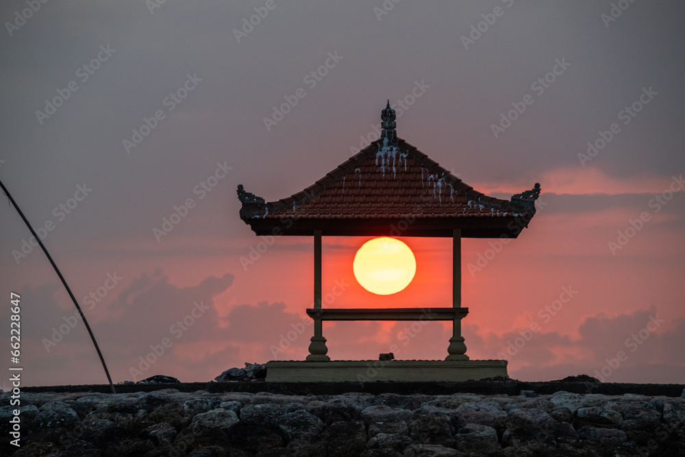 Great sun ball in a small temple in Bali, on the sandy beach of Sanur. Sun ball on the horizon and clouds in the sky. Everything in the morning over the sea of Indonesia Great sun ball in a small temple in Bali, on the sandy beach of Sanur. Sun ball on the horizon and clouds in the sky. Everything in the morning over the sea of Indonesia