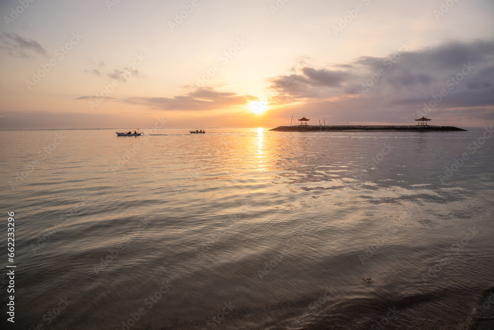 Sunrise at the sandy beach of Sanur. Temple in the water. Traditional fishing boat, Jukung on the beach. Hindu faith in Sanur on Bali. Dream island and dream destination