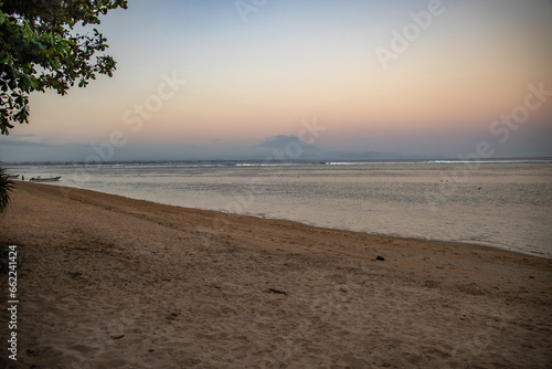 Beautiful sunrise on Sanur beach. Temple in the calm sea. Small waves in the morning. Sandy beach on the dream island of Bali. in the background the volcano Mount Agung