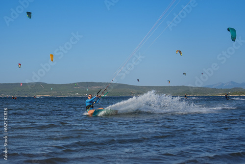 Beautiful girl with blond hair kitesurfing in blue sea splashing water with kites in the background