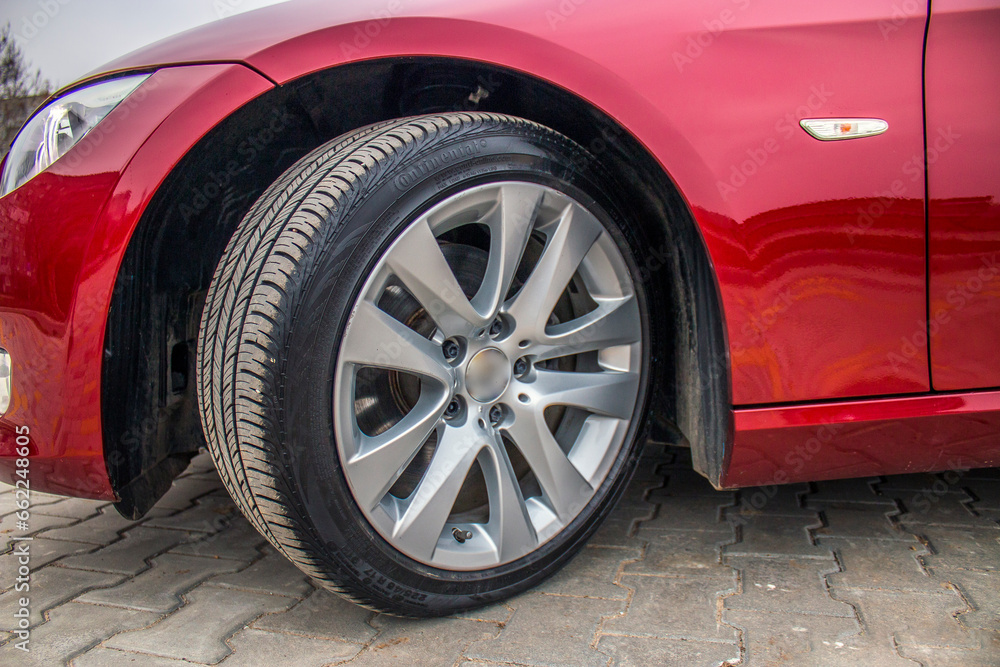 Gray car rim on a turned wheel of a red car