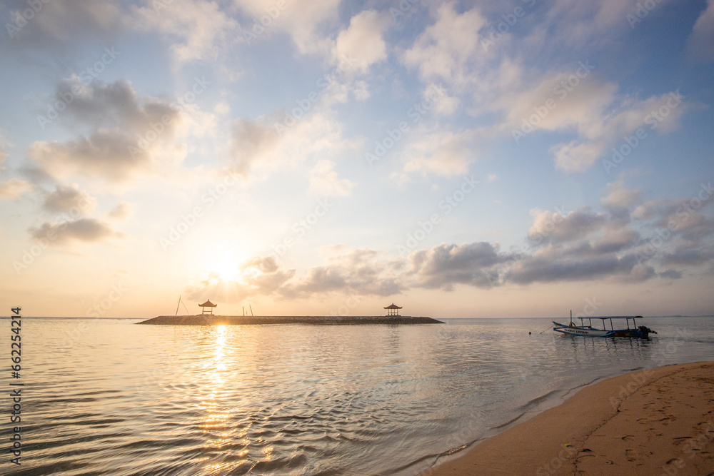 Sunrise in Bali. The beach of Sanur with a fishing boat, jukung. Landscape shot with temple in the sea. view from the sandy beach into the horizon
