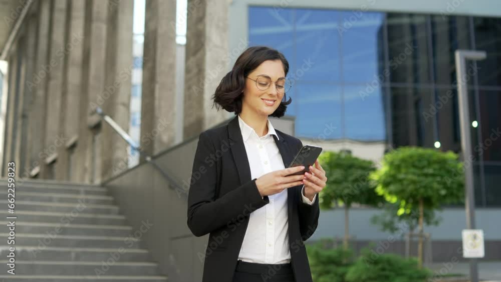 Young smiling businessman in formal suit is using a smartphone walking on the street near office building. Happy brunette female student looking at screen, reading received message on mobile phone Young smiling businessman in formal suit is using a smartphone walking on the street near office building. Happy brunette female student looking at screen, reading received message on mobile phone