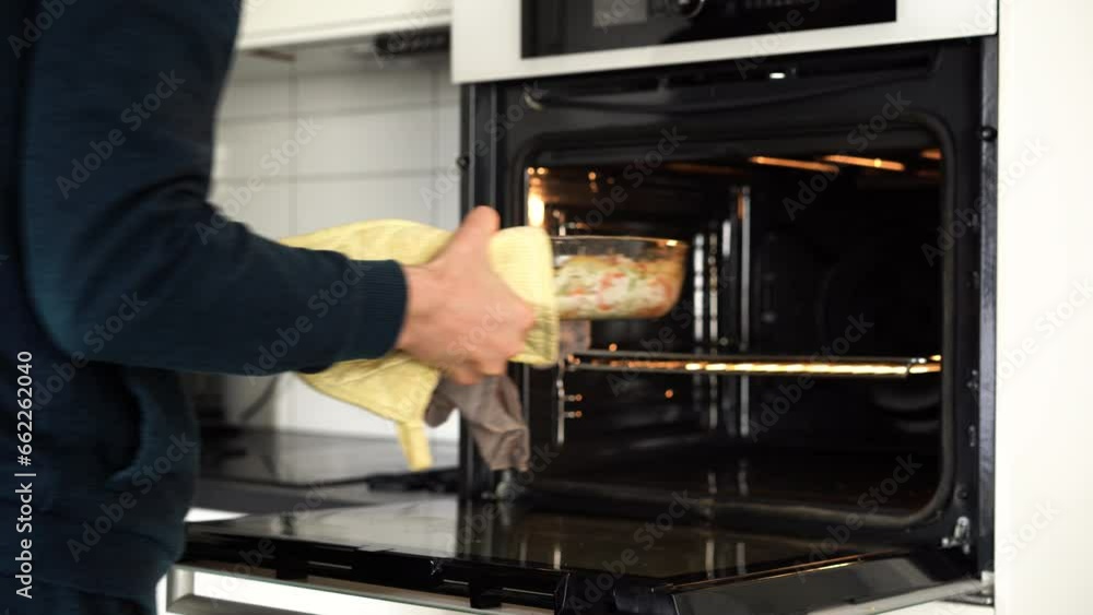 A man takes a dish of fish and vegetables out of the oven A man takes a dish of fish and vegetables out of the oven