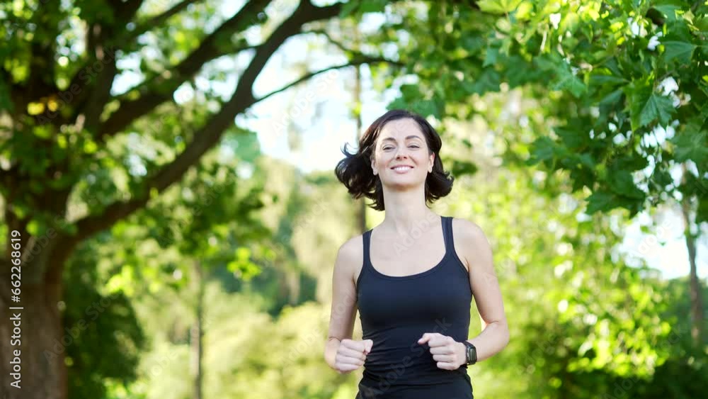Young female runner jogging in an urban city park. Happy brunette sportswoman enjoys jogging outdoors. A cute fit woman in a black tracksuit is doing her morning run. Training workout in nature Young female runner jogging in an urban city park. Happy brunette sportswoman enjoys jogging outdoors. A cute fit woman in a black tracksuit is doing her morning run. Training workout in nature