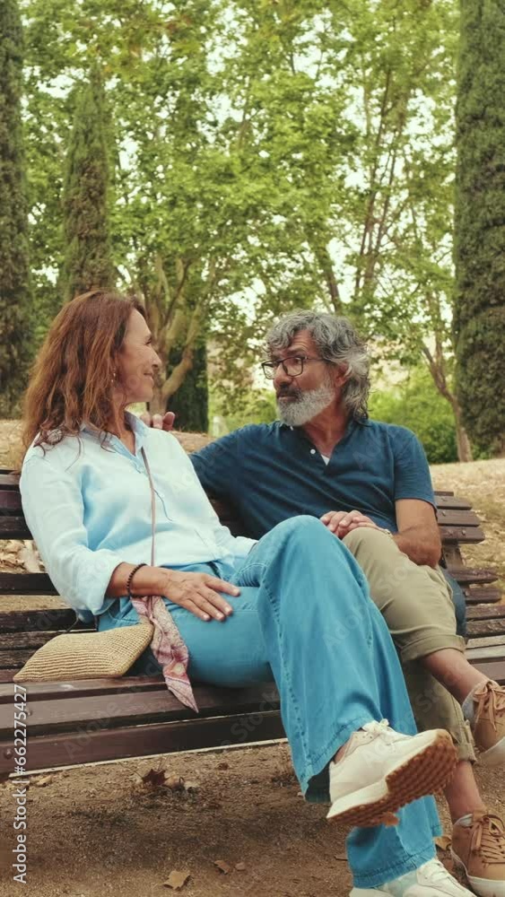 Happy elderly couple talking while sitting on park bench Happy elderly couple talking while sitting on park bench