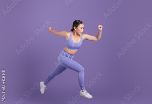 Young asian woman in sportswear running over purple studio background, free space