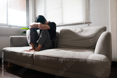 Man with mental health problem sitting on couch to resting head on his arms with depressed emotion