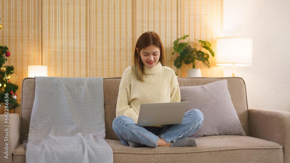 Winter season concept, Women use laptop to shopping online and sitting on couch near christmas tree Winter season concept, Women use laptop to shopping online and sitting on couch near christmas tree