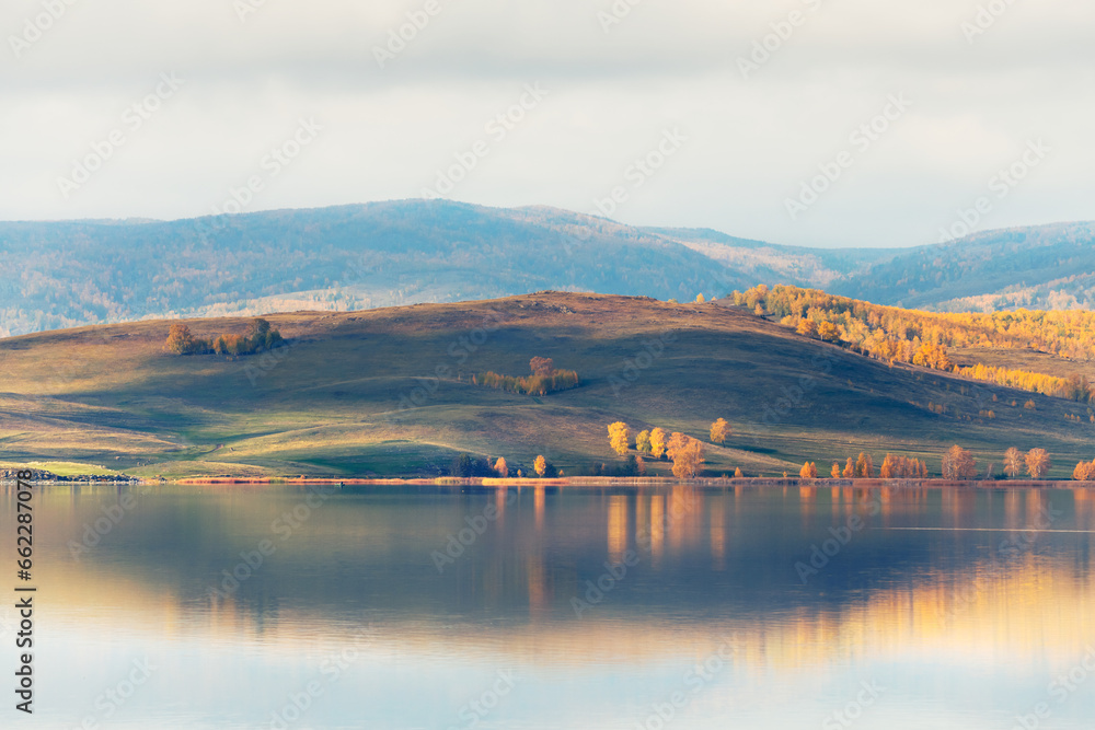 Lake in the autumn mountains. Yellow trees and mountains are reflected in the lake at sunrise.