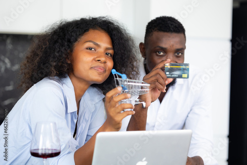 online shopping, credit card mockup. Young happy african amerian couple using laptop and credit card while shopping online on internet at home. Kitchen room photo