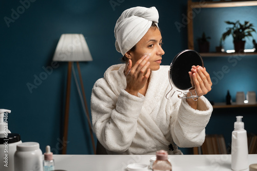 Obraz na plátně Beautiful hispanic woman applying face cream sitting at the table