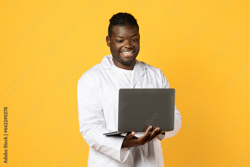 African american man doctor working on laptop over yellow background African american man doctor working on laptop over yellow background