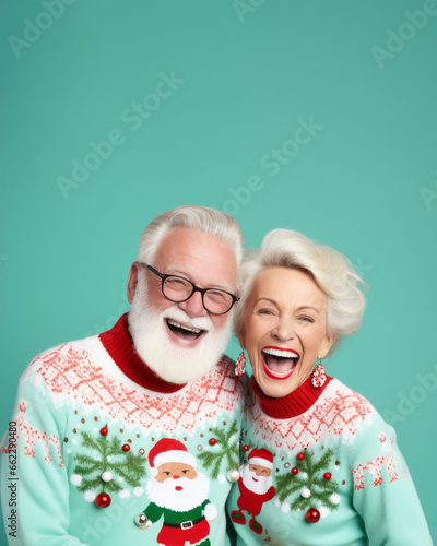 An older couple donning festive sweaters adorned with christmas motifs smile and laugh happily, their glasses glinting in the indoor light as they stand against a wall, joy  of the holiday season photo
