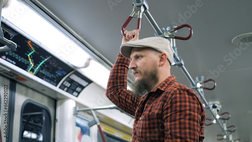 Millennial in cap holding handrail of underground subway. Close-up of tired man staggers in subway holding handrail so as not to fall. Use handrail in subway to avoid falling when car wobbles at speed photo