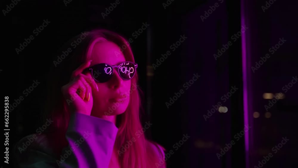 Beautiful girl takes glasses in her hands. Reflection of a neon sign in glasses. Beautiful girl takes glasses in her hands. Reflection of a neon sign in glasses.