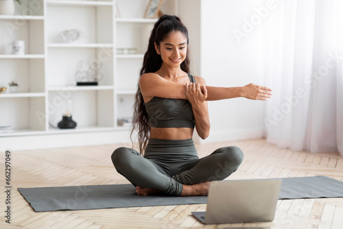 Happy indian woman exercising with trainer online via laptop
