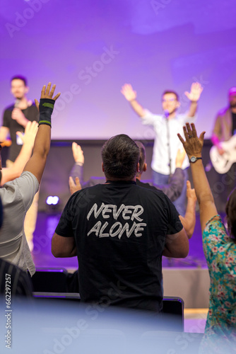 Man with his hands raised to prayer in the church, having a t -shirt with the message never alone